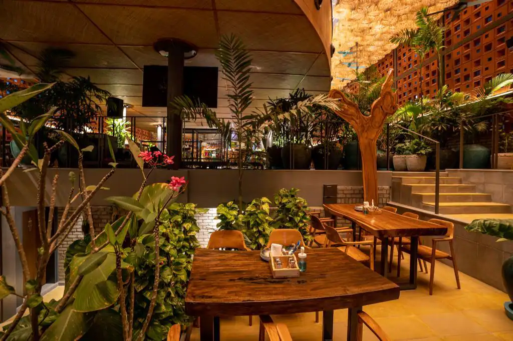 The dining floor by day: live-edge timber tables, a driftwood sculpture and the terracotta jaali wall behind the bar.